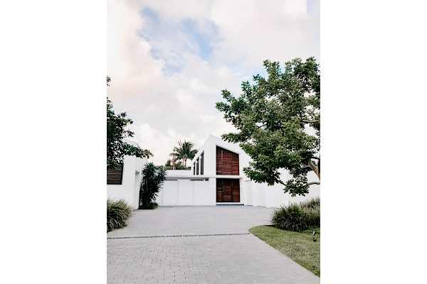 A white house with a red door and a tree in front.